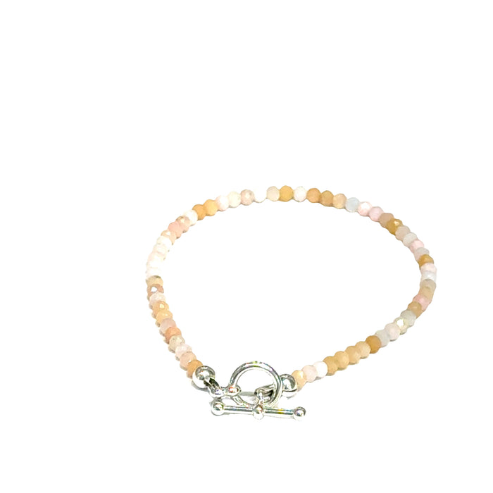 Close-up of faceted pink opal gemstone beads on delicate beaded bracelet with handcrafted toggle on a white background, back toggle view.