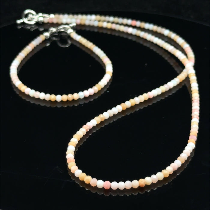 Close-up of faceted pink opal gemstone beads on delicate beaded bracelet with handcrafted toggle with its matching necklace on a black background, front view.