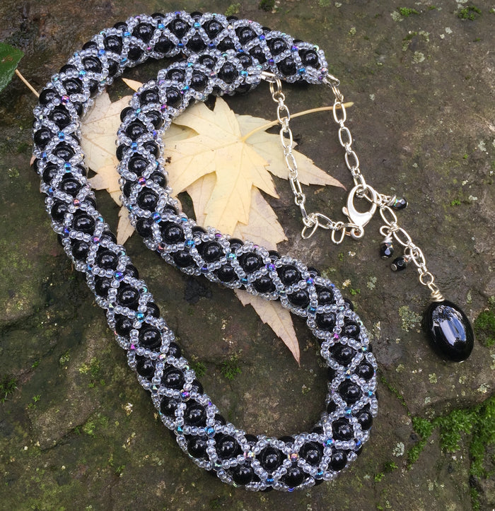 This fancy Black and Multi Iridescent Netted Treasure Necklace is held together by crystal and iridescent seed beads, which give it a subtle flash. The tail ends with three Swarovski crystals and a smooth black oval bead. This necklace is adjustable and can be worn from 20 1/2" to 23".