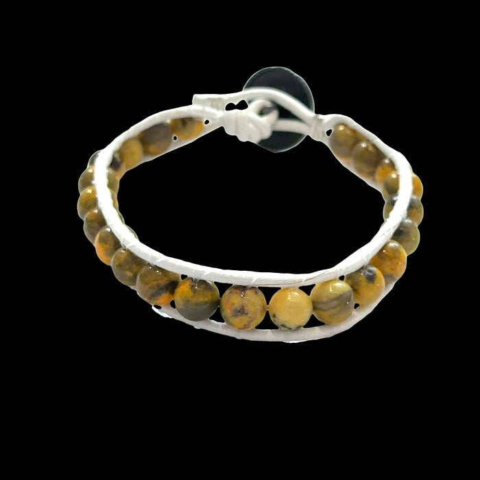 Close-up of genuine Bumblebee Jasper beads showing vibrant yellow and black volcanic patterns, 6mm gemstone bracelet, on a black background, font view.