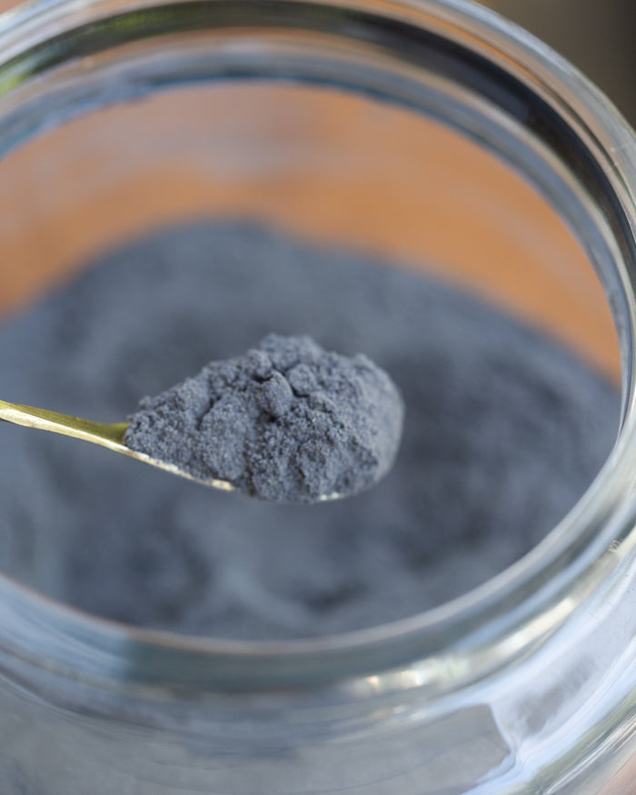 Spoonful of dark gray powder over a glass container