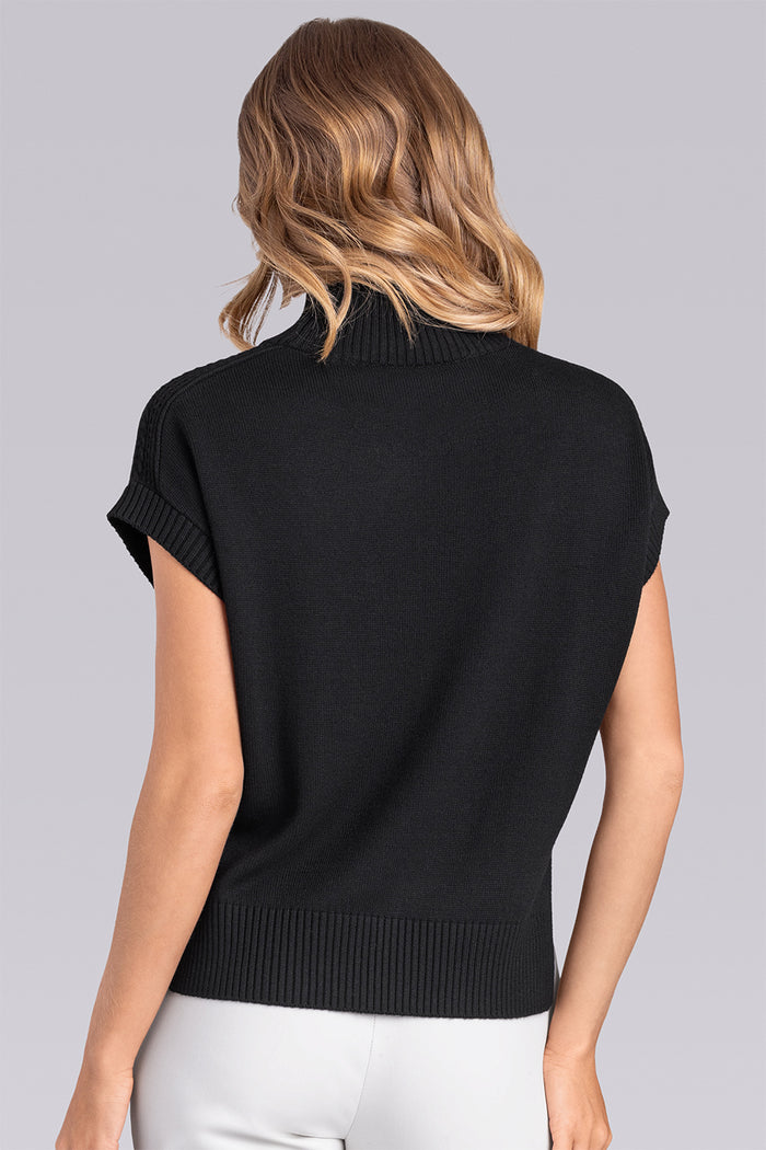 Model wearing the Charisma Black short sleeve knit shirt, styled with white pants.
