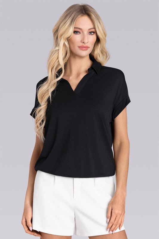 Model wearing the Conquest Black short sleeve notched neck shirt, styled with white shorts.