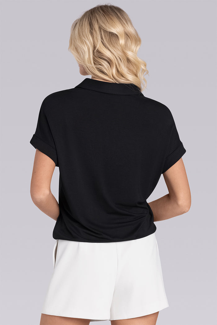 Model wearing the Conquest Black short sleeve notched neck shirt, styled with white shorts.