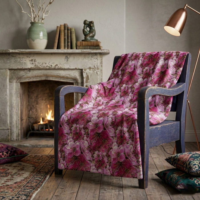 Crushed velvet blanket with a vibrant pink and white cherry blossom floral pattern, shown draped over a wooden armchair.