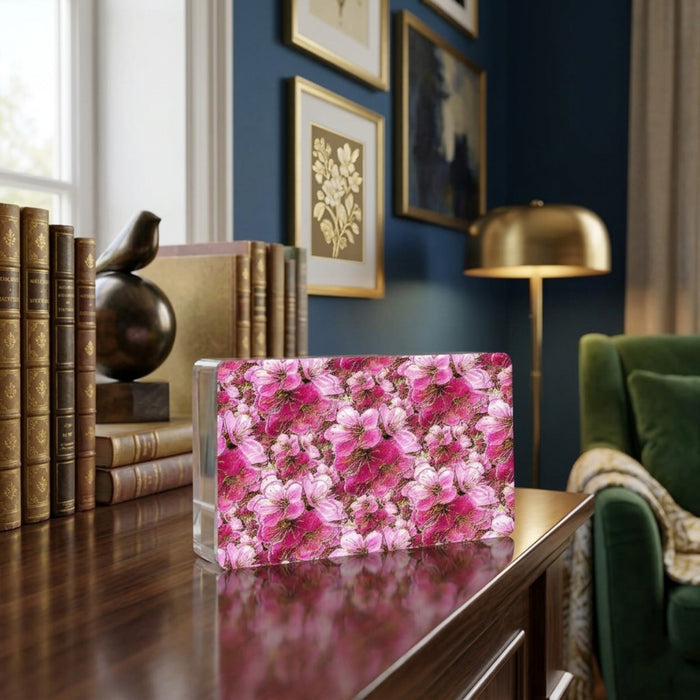 Modern acrylic block featuring a vibrant pink floral pattern, displayed on a wooden table in a sophisticated library setting with books and a green armchair.