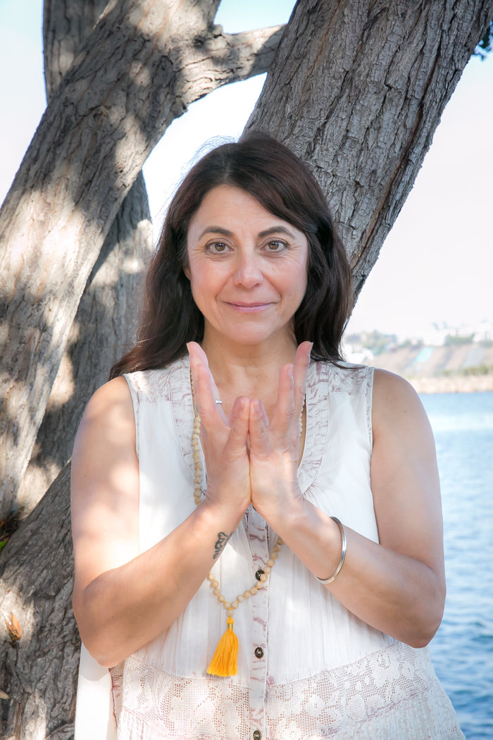 Woman with hands clasped in front of a tree and body of water