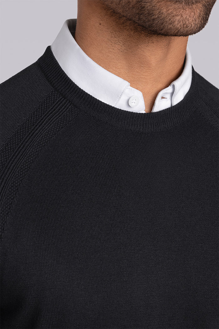 Model wearing Exemplary Black raglan sleeve crewneck sweater, styled with light grey slacks.