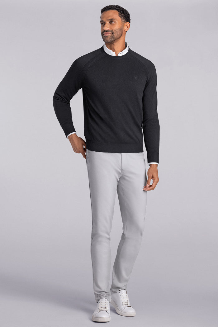 Model wearing Exemplary Black raglan sleeve crewneck sweater, styled with light grey slacks.