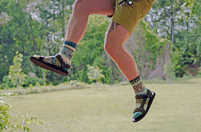 Person jumping outdoors wearing mismatched goat pattern crew socks