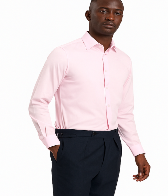 Man wearing a light pink dress shirt and dark pants on a white background