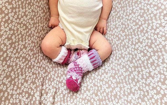 Baby wearing soft pink patterned socks while lying on floral blanket