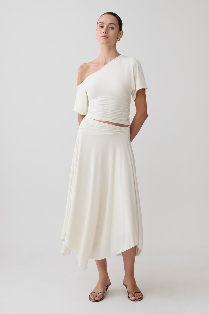 Woman wearing a white one-shoulder top with a matching midi skirt.