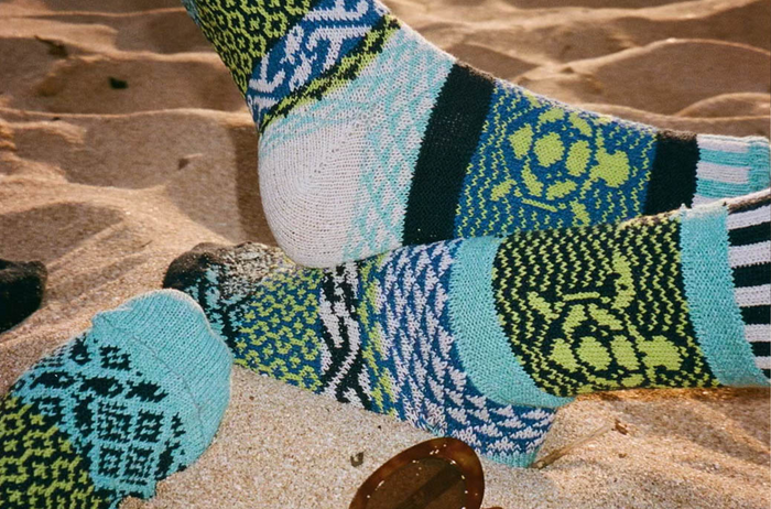 Ocean pattern mismatched crew socks displayed on sandy beach surface