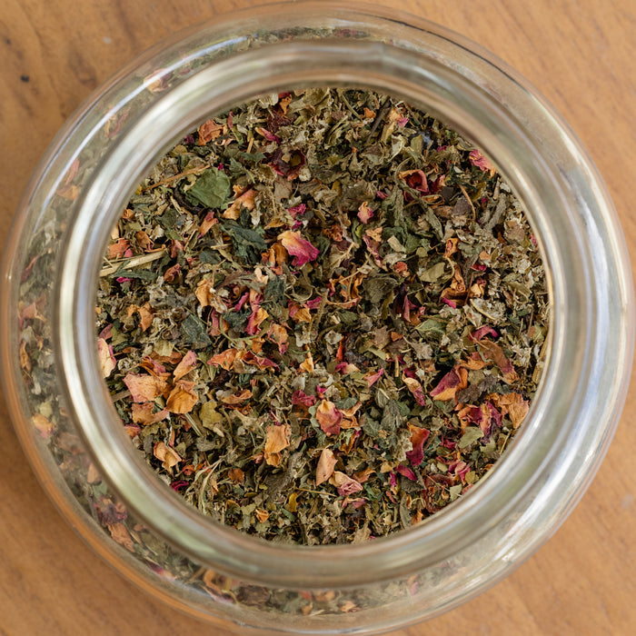 Clear glass jar filled with dried herbs on a wooden surface