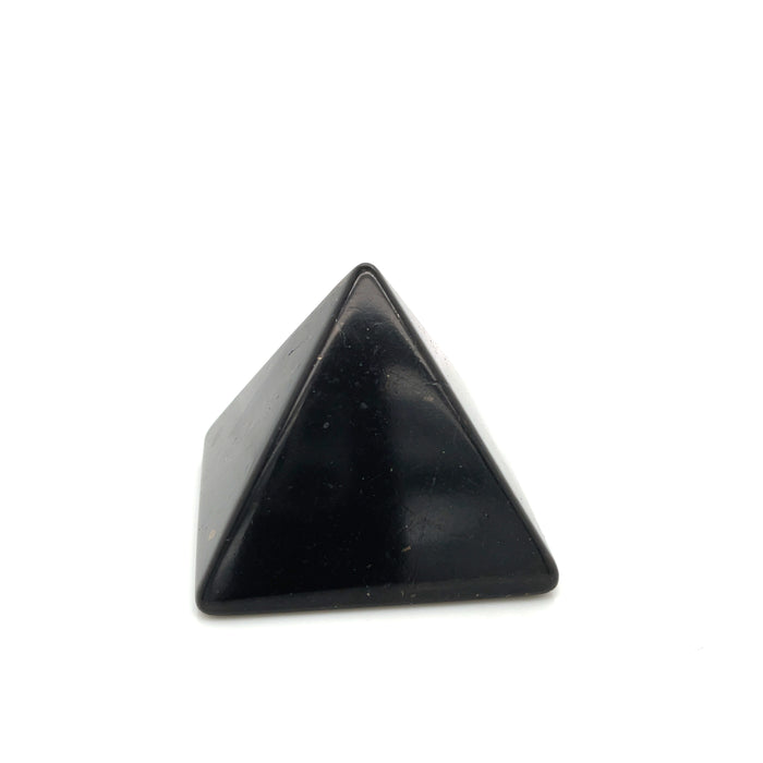 One small shungite pyramid on desk near computer for radiation blocking on a white background, front view.