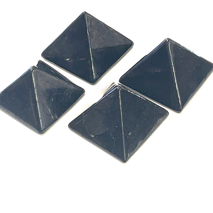 Four small shungite pyramid on desk near computer for radiation blocking on a white background, front view.