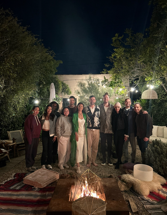 Group of people posing outdoors at night with a fire pit and decorative lights.