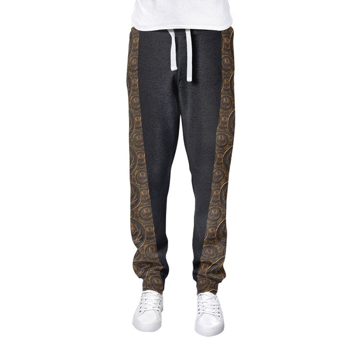 Isolated front view of men's dark grey joggers featuring structured white drawstrings and ornate antiqued bronze medallion patterns on the side panels.