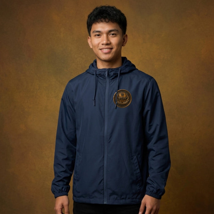 Front view of a man against a studio backdrop wearing a navy blue windbreaker with an antiqued bronze Paleo-Hebrew script emblem on the left chest.