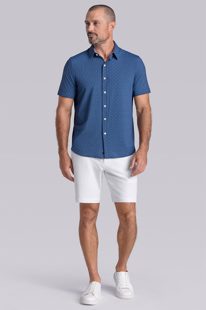 Model wearing Synergy Classic Blue 6-way knit® short sleeve classic collar shirt, styled with white shorts.