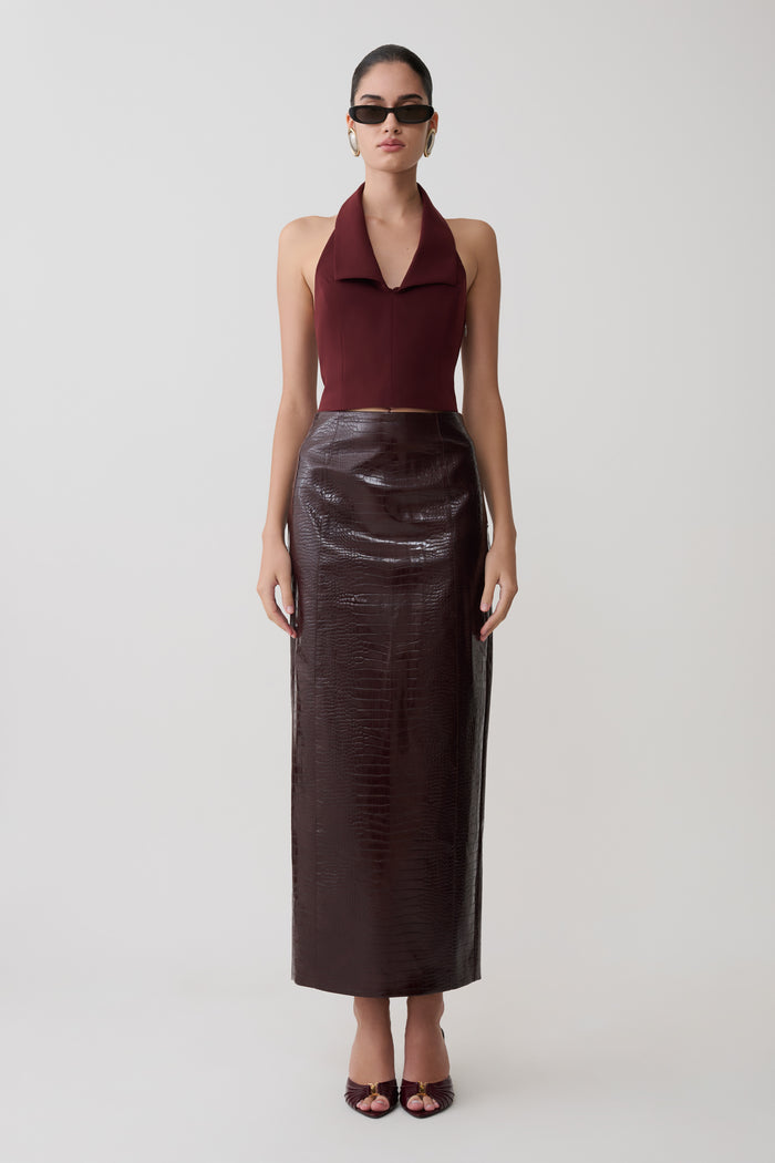 Woman wearing a burgundy halter top and dark brown leather skirt on a white background.