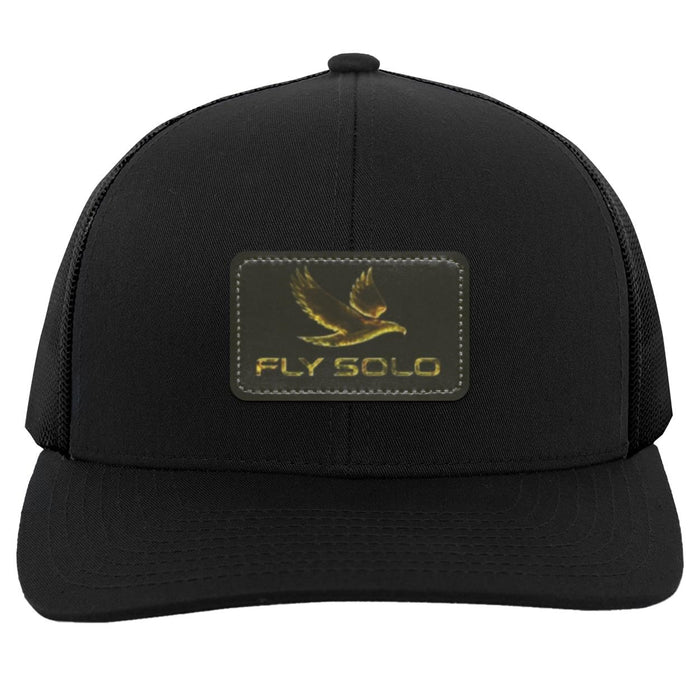 Clean front product shot of the solid black Fly Solo trucker hat with gold embossed branding.