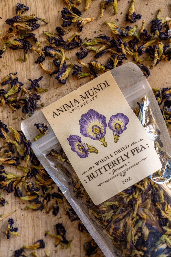 Packaged butterfly pea flowers with Anima Mundi Apothecary label on a wooden surface.